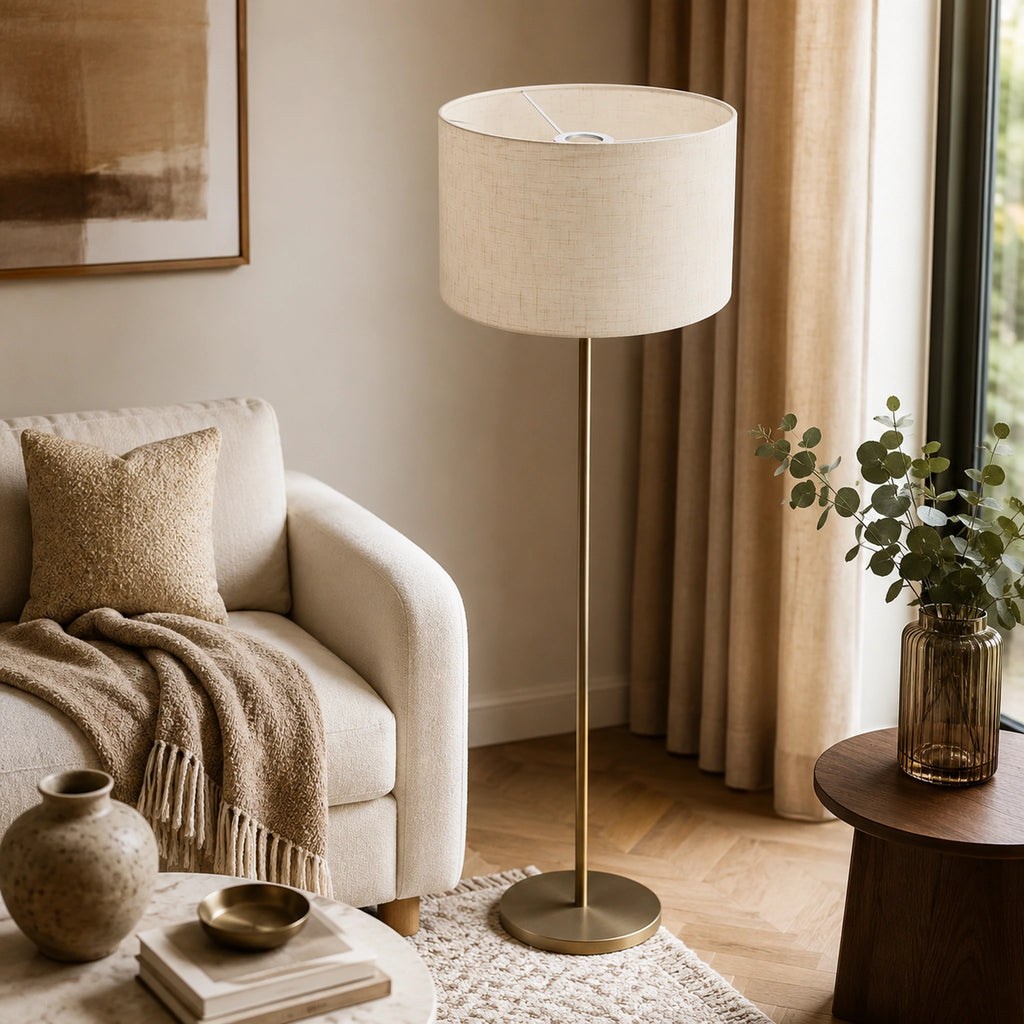 Abat-jour en lin naturel monté sur un lampadaire à pied laiton doré dans un salon chaleureux aux tons beiges