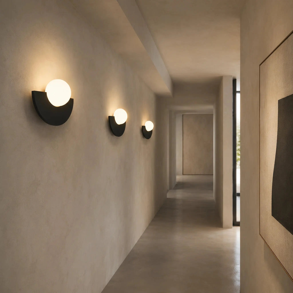 Série d'abat-jour muraux noirs en demi-lune avec boule en verre dépoli alignés dans un couloir minimaliste
