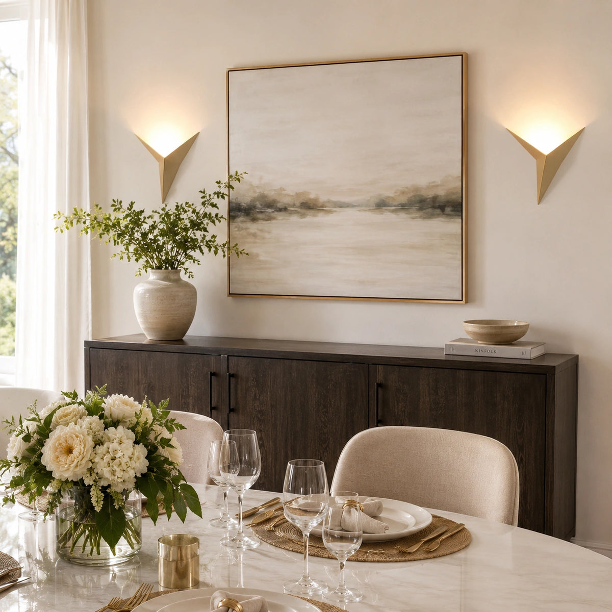 Deux abat-jour muraux origamis dorés encadrant un tableau dans une salle à manger chic dressée pour un dîner élégant