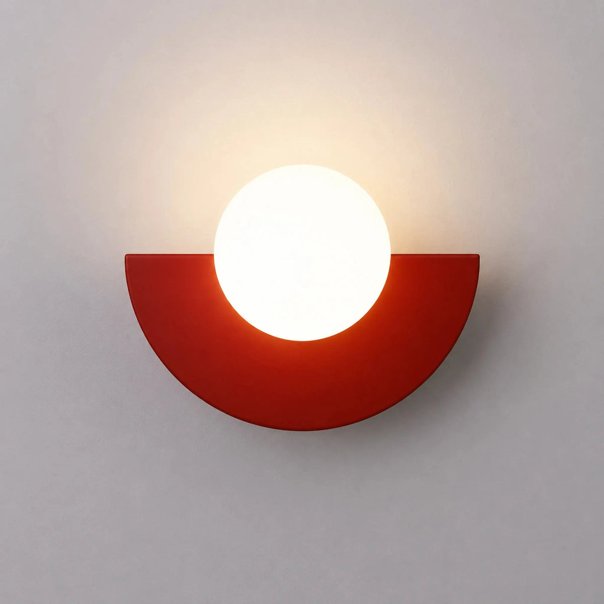 Abat-jour mural rouge en demi-lune avec boule en verre dépoli allumée, vue de face sur fond neutre