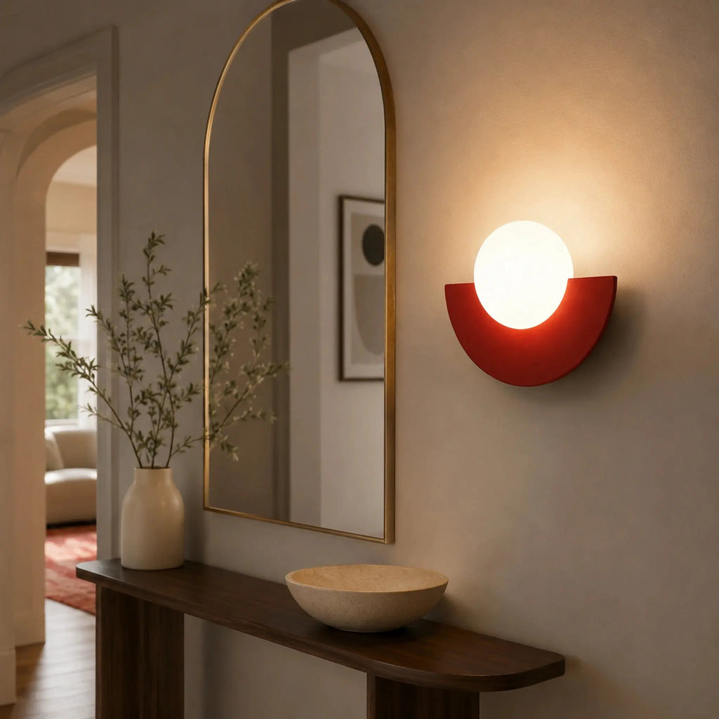 Abat-jour mural rouge en demi-lune avec boule en verre dépoli dans une entrée élégante avec miroir doré