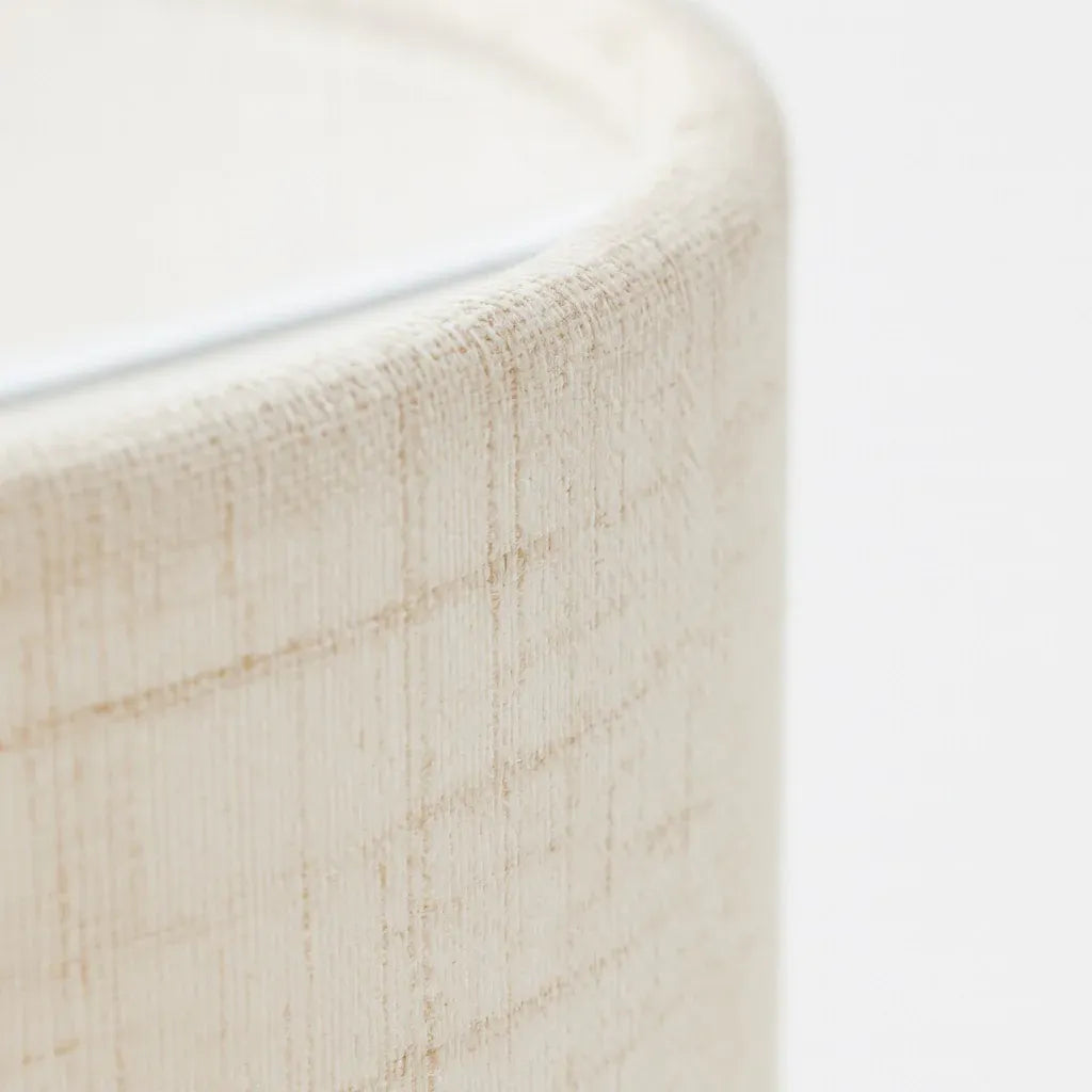 Gros plan sur la texture tissée du lin beige de l'abat-jour tambour, détail matière naturelle et artisanale