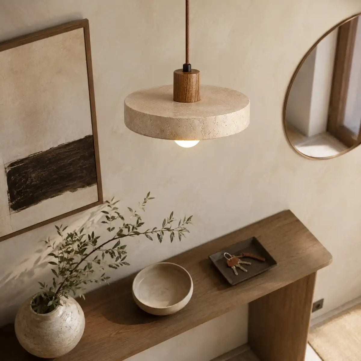 Abat-jour en travertin plat suspendu au-dessus d'une console en bois dans une entrée aux tons naturels avec miroir rond